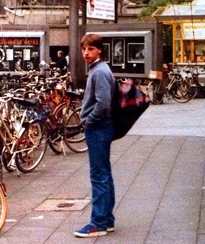 1980s casual in a crew-neck jumper, jeans and trainers with a holdall over his shoulder